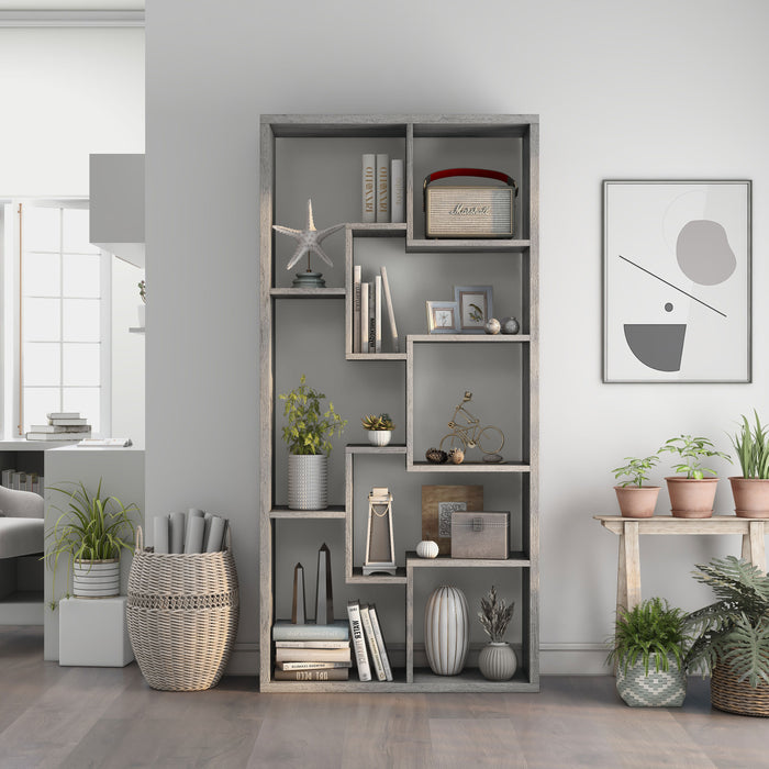Front-facing modern vintage gray oak geometric bookcase with staggered shelves in a living area with accessories