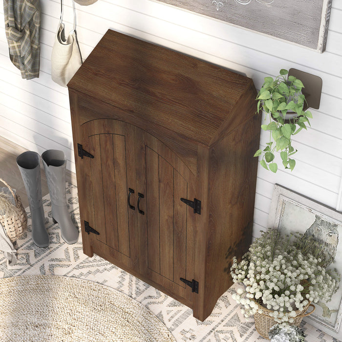 Left-facing top-down view of transitional distressed walnut finish shoe cabinet in a country farmhouse style entryway foyer. Adjustable shelves behind two plank style doors and flip top shelf. Rustic black door pulls and black hinges.