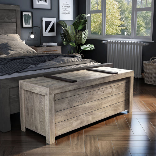 Right angled rustic weathered oak storage bench with a sliding top at the foot of a bed with accessories