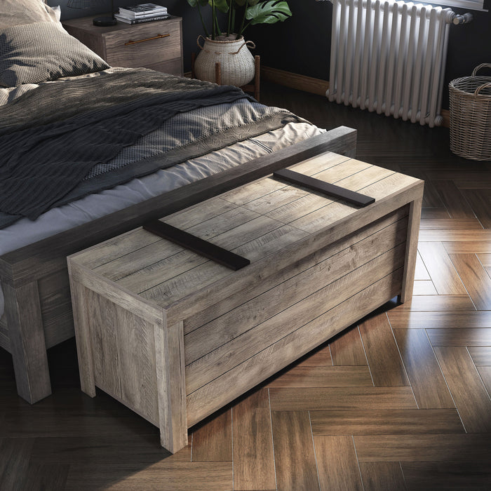 Right angled bird's eye view of a rustic weathered oak storage bench with a sliding top at the foot of a bed with accessories