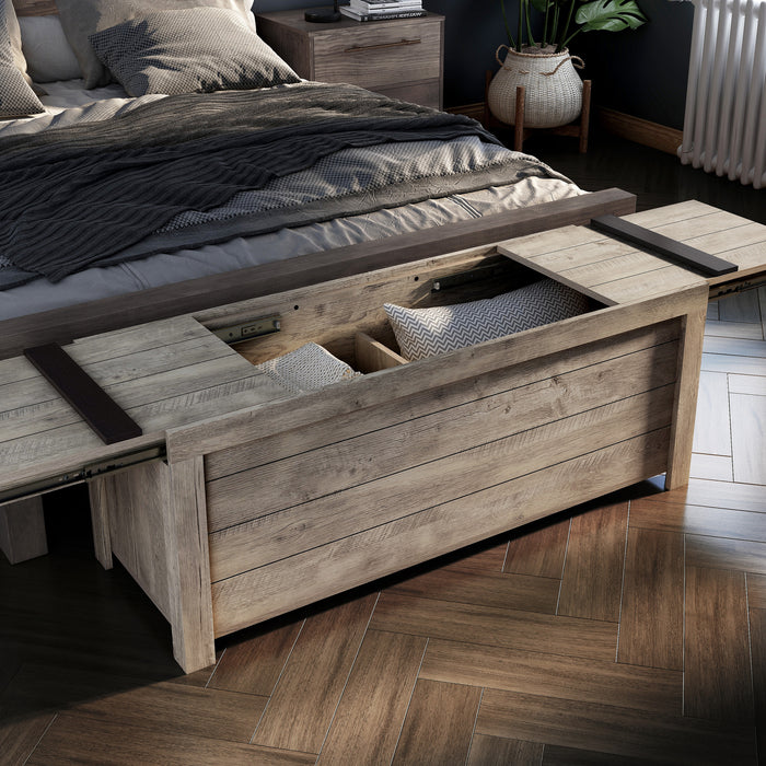 Right angled bird's eye view of a rustic weathered oak storage bench with its sliding top open at the foot of a bed with accessories