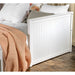 Left angled close up cottage style white daybed with three drawers outer side detail in a living space with linens and accessories