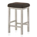 Left-facing view of rustic antique white counter height stool with dark brown fabric seat on a white background