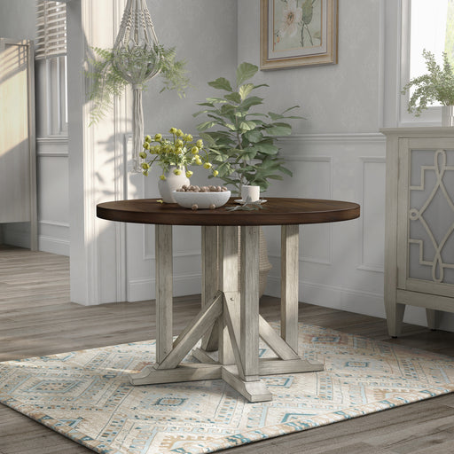 Right angled view of rustic dark oak round dining table with an antique white trestle pedestal base in a dining room with decor