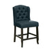 Left-angled navy blue counter-height chair against a white background. The button-tufted wingback chair and seat are accented in nailhead trim. An antique black leg frame offers footrests for comfort and rustic style.