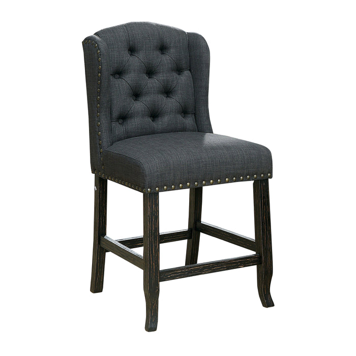 Right-angled dark grey counter-height chair against a white background. The button-tufted wingback chair and seat are accented in nailhead trim. An antique black leg frame offers footrests for comfort and rustic style.