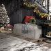 Grey upholstered and skirted bench under a black matte staircase. A red square throw pillow decorates the bench, while a light Christmas tree and garland on the stair railing adorns its surrounding.
