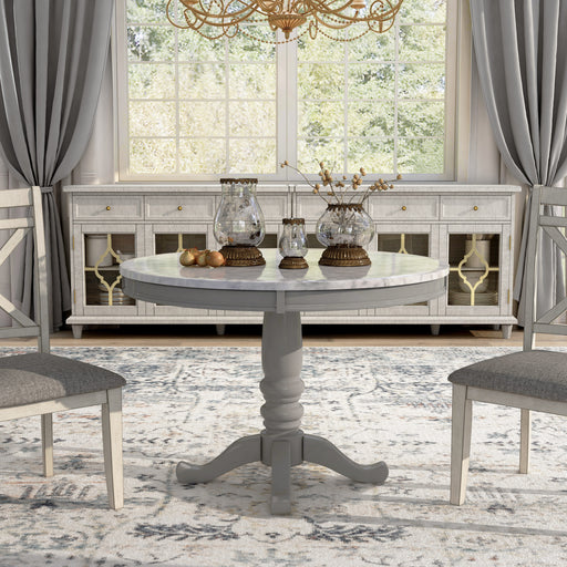 Front-facing contemporary round pedestal dining table with a white faux marble top in a dining room with accessories