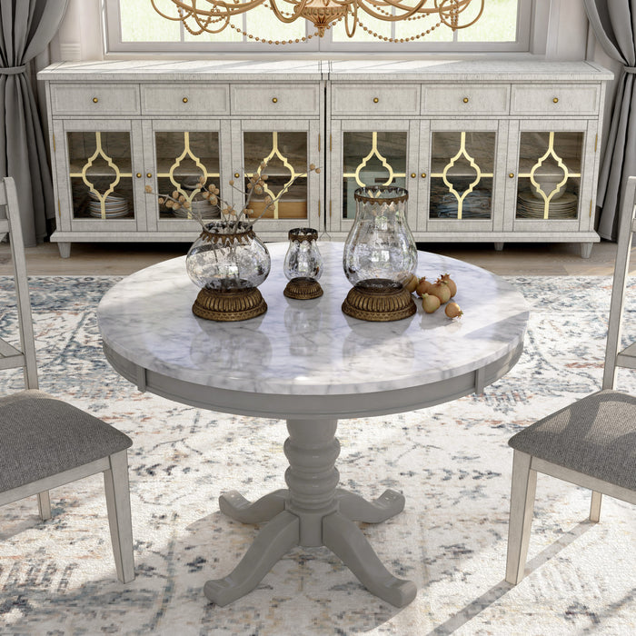 Front-facing contemporary round pedestal dining table with a white faux marble top in a dining room with accessories