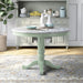 Front-facing contemporary olive green pedestal dining table with a white faux marble top in a dining room with accessories