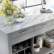 Right angled top-down view of white marble-like tabletop and drawer storage of farmhouse light gray counter height table with decor in a kitchen