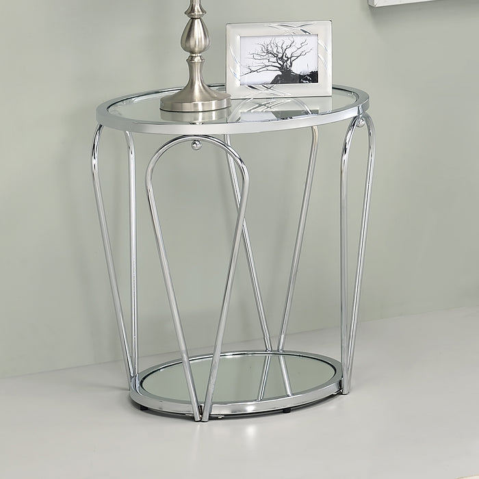 Right angled modern round chrome end table with open teardrop shape steel legs, a clear tempered glass top, and mirror open bottom shelf decorated with lamp against a wall.