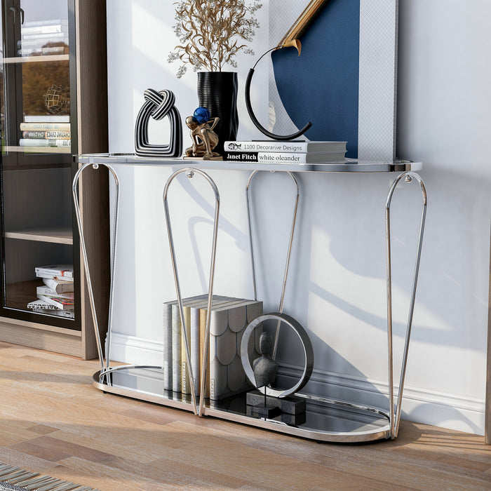 Left angled modern chrome console table with open teardrop shape steel legs, rounded tempered glass top, and mirror open bottom shelf with books and decor in living room setting.