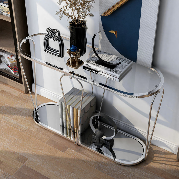 Left angled top-down modern chrome console table with open teardrop shape steel legs, rounded tempered glass top, and mirror open bottom shelf with books and decor against wall.