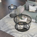 Right angled top-down view of modern round black nickel coffee table and end table with teardrop legs and mirrored lower shelf with decor next to living room sofa