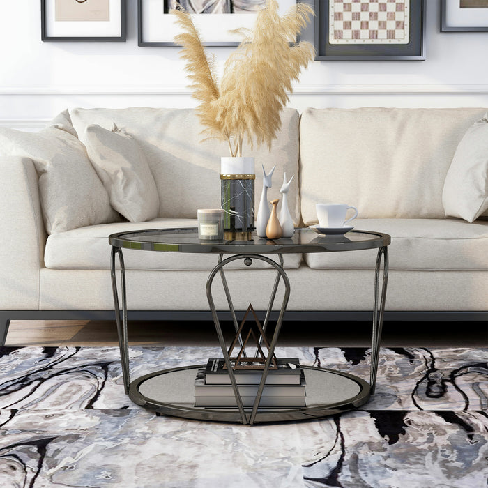 Front-facing modern round black nickel coffee table with open teardrop shape steel legs, a gray tempered glass top, and mirror open bottom shelf decorated with accessories on a rug in front of a sofa.
