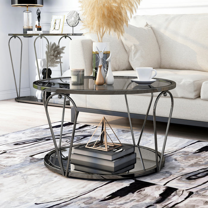 Left angled modern round black nickel coffee table with open teardrop shape steel legs, a gray tempered glass top, and mirror open bottom shelf with matching console table in background in a living room.