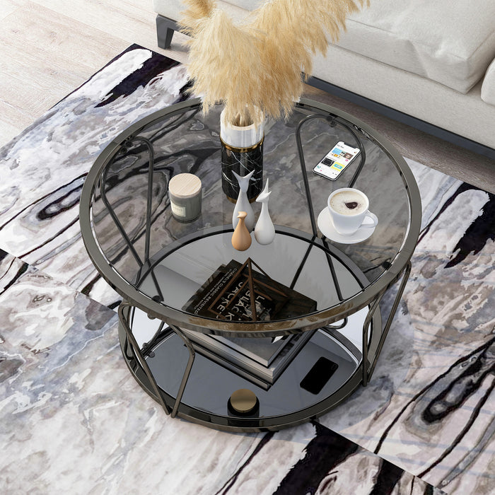 Left angled top-down modern round black nickel coffee table with open teardrop shape steel legs, a gray tempered glass top, and mirror open bottom shelf decorated with books and accessories on a rug.