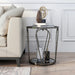 Front-facing modern round black nickel end table with open teardrop shape steel legs, a gray tempered glass top, and mirror open bottom shelf decorated with books and accessories next to a sofa.