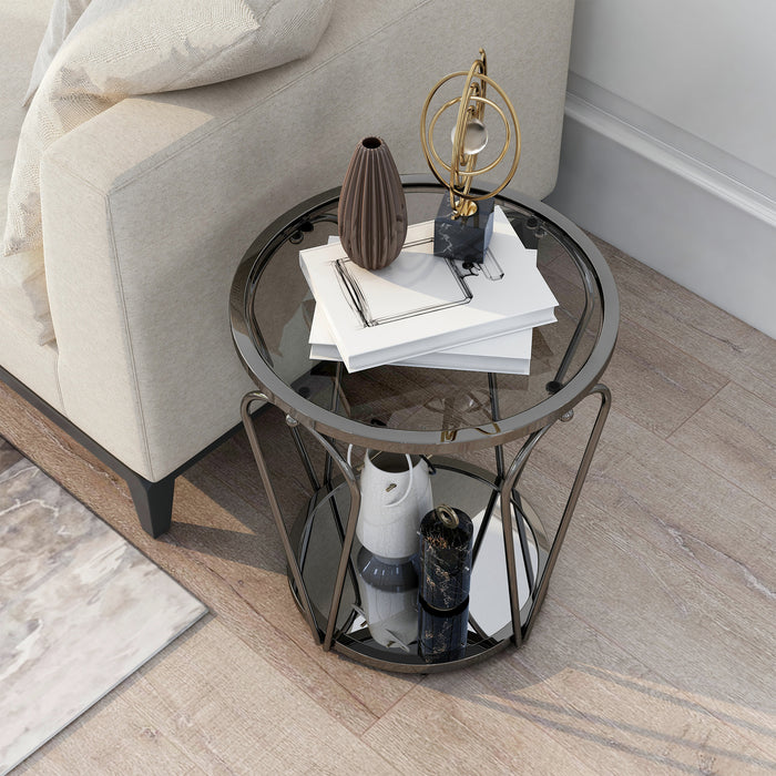 Left angled top-down modern round black nickel end table with open teardrop shape steel legs, a gray tempered glass top, and mirror open bottom shelf decorated next to a sofa.