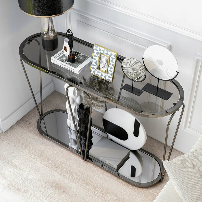 Left angled top-down modern black nickel console table with open teardrop shape steel frame, a rounded gray tempered glass top, and mirror open bottom shelf decorated and set against wall.