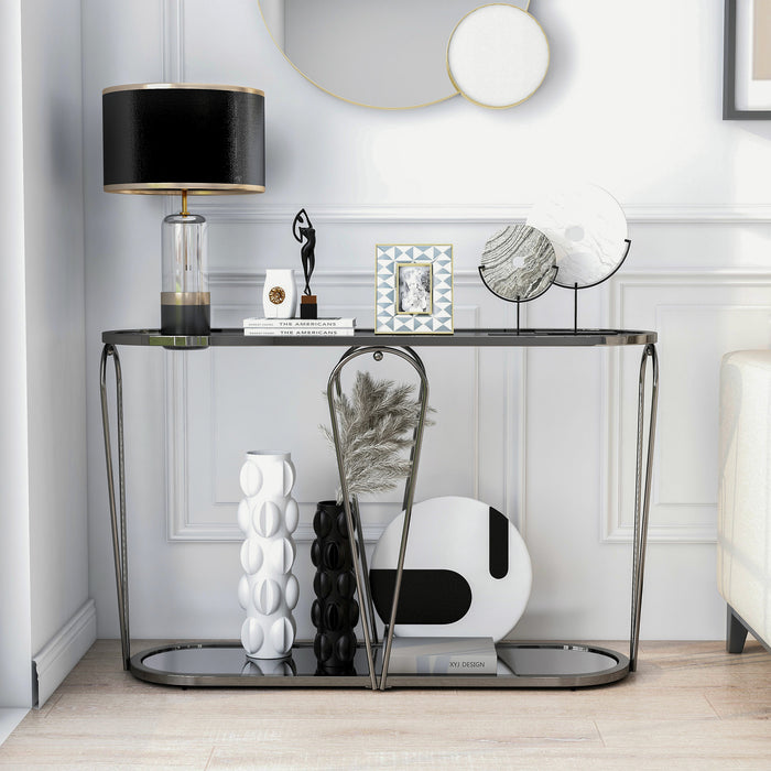 Front-facing modern black nickel console table with open teardrop shape steel frame, a rounded gray tempered glass top, and mirror open bottom shelf decorated with art and lamp against wall.