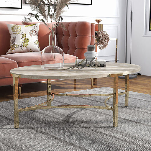Right angled view of modern glam oval coffee table with white faux marble tabletop and champagne steel base decorated in front of a living room sofa