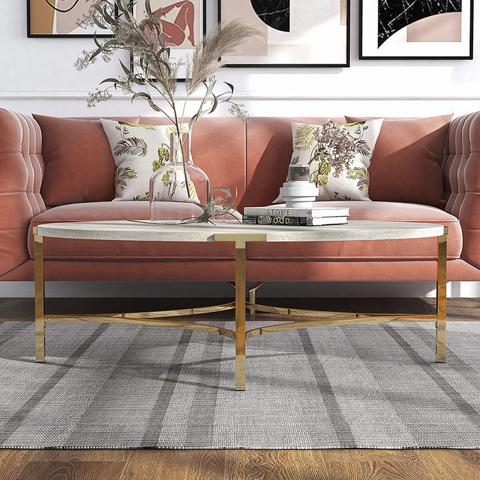 Front-facing view of modern glam oval coffee table with white faux marble tabletop and champagne steel base decorated in front of a living room sofa
