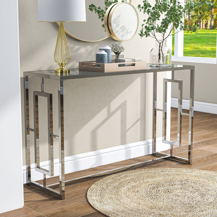 Right angled view of modern chrome plated steel sofa table with geometric trestle base and waterfall pattern tempered glass top decorated in a living room