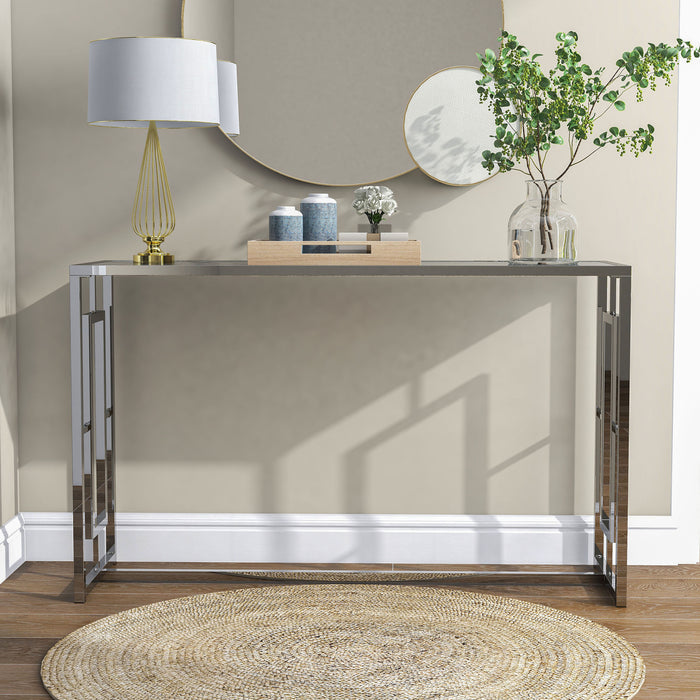 Front-facing view of modern chrome plated steel sofa table with geometric trestle base and waterfall pattern tempered glass top decorated in a living room