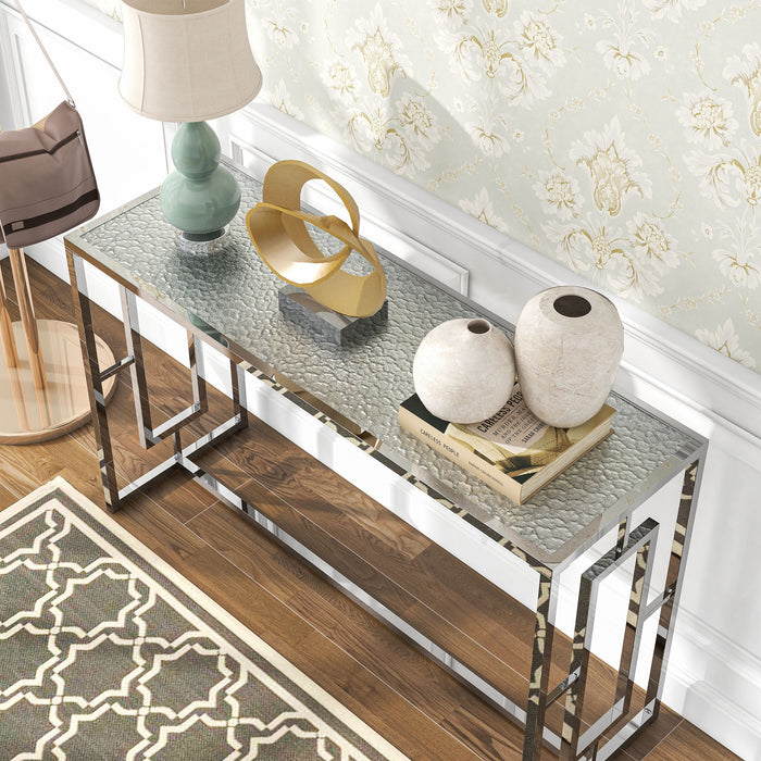 Left angled top-down view of modern chrome plated steel sofa table with geometric trestle base and water rippled tempered glass top decorated in a living room