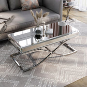 Left angled view of contemporary glam chrome finish steel and mirror coffee table in living room with accessories and parts of matching pieces.