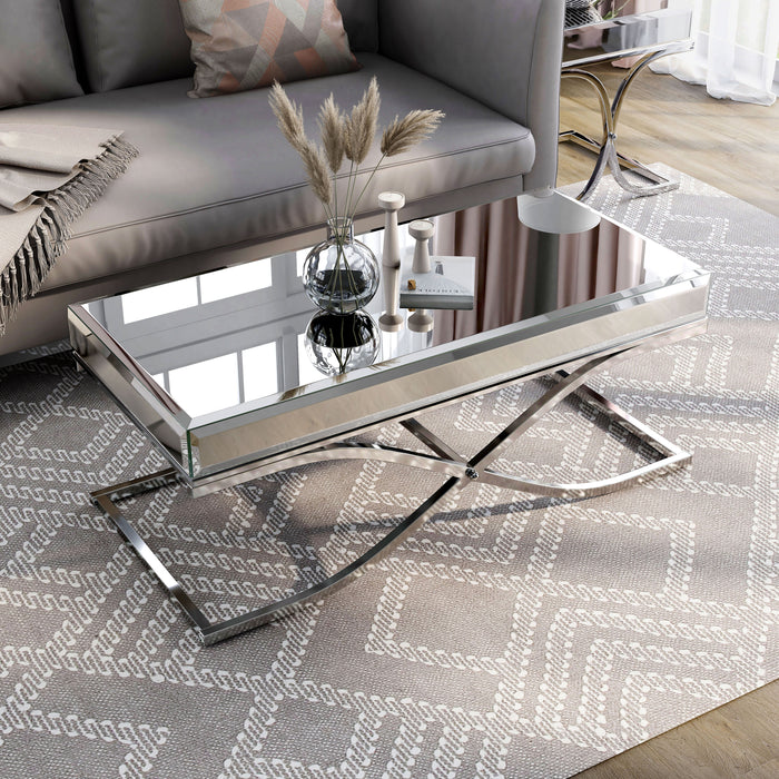 Left angled view of contemporary glam chrome finish steel and mirror coffee table in living room with accessories and parts of matching pieces.