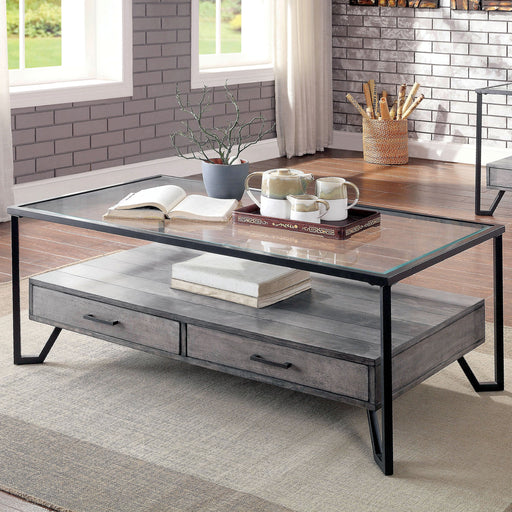 Left angled industrial two-drawer coffee table in a living room with decor accessories. Smooth glass top and spacious lower shelf with plank details rests on a black angled metal frame. 