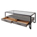 Left angled industrial two-drawer coffee table with opened drawers on a white background. Glass top and spacious plank style lower shelf rest on a black angled metal frame.