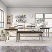 Semi-side facing view of transitional three-piece antique white and brown finish wood coffee table set in living room with accessories