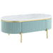 Right-facing glam light teal fluted coffee table with oval faux white marble top and gold accents on white background. Single flush drawer and trestle legs.
