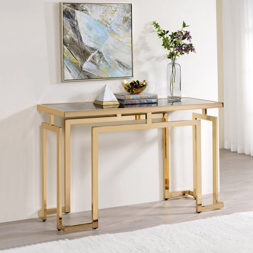 Right angled contemporary gold steel console table with accessories placed against a wall. Tempered glass top and geometric base design lends sleek look.