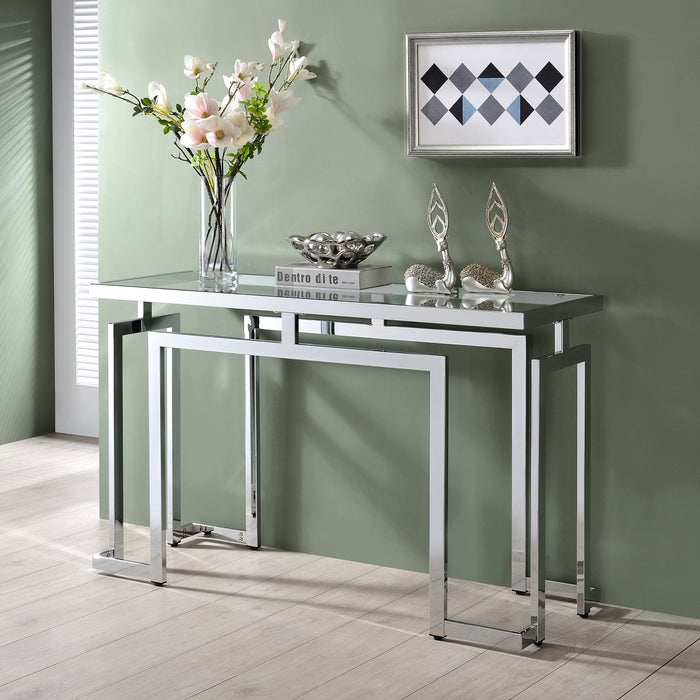 Left angled contemporary chrome steel console table with accessories placed against a wall. Tempered glass top and geometric base design lends sleek look.