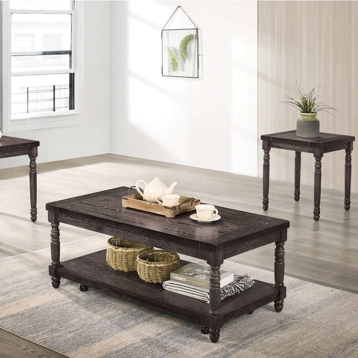 Left angled contemporary gray wood coffee table and two matching end tables in a living room setting. Carved legs and wood plank tabletops offer a rustic touch. Open bottom shelf on coffee table offers extra storage.