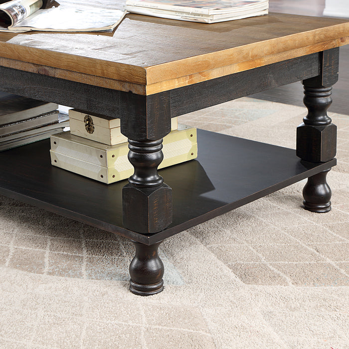 Left angled rustic antique black wood coffee table detail of oak tabletop, traditional carved legs and decorated open bottom shelf on a rug.