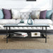 Front-facing modern industrial black steel coffee table with tempered white marble glass top, slender steel legs and perforated open metal shelf with decor in front of a sofa.
