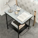 Left angled top-down modern industrial black steel end table with tempered white marble glass top, slender steel legs and perforated open metal shelf decorated with books and table lamp next to a sofa.