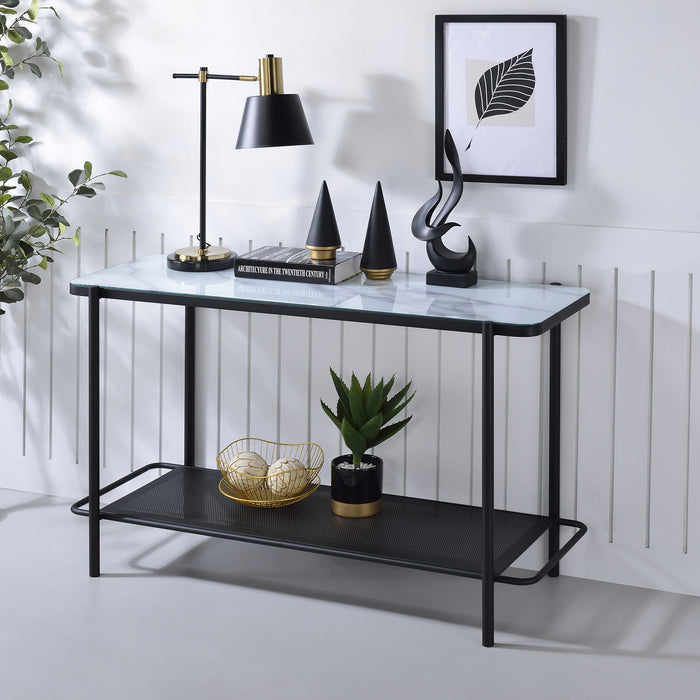 Left angled modern industrial black steel console table with tempered white marble glass top, perforated open metal shelf, and slim legs with lamp and decor against a wall.