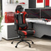 Angled view of contemporary red and black faux leather and metal gaming chair in work space with furnishings and accessories