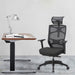 Left angled contemporary black adjustable office chair with headrest in an office with accessories