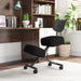 Left angled modern black ergonomic kneeling chair with wheels at a desk with accessories