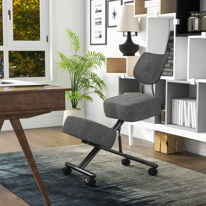 Left angled modern gray ergonomic kneeling chair with wheels at a desk with accessories