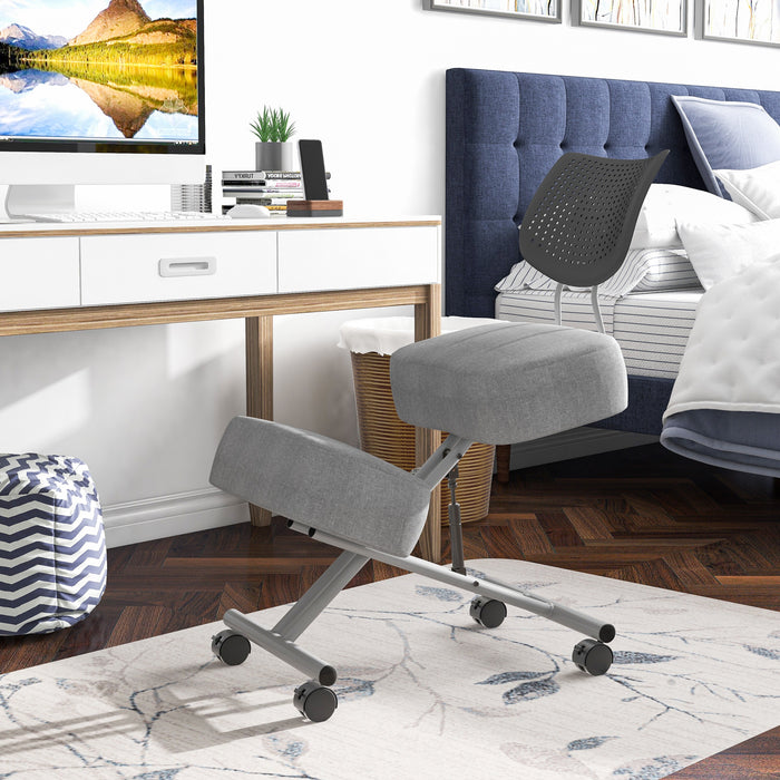 Left angled modern light gray ergonomic kneeling chair with wheels at a desk with accessories