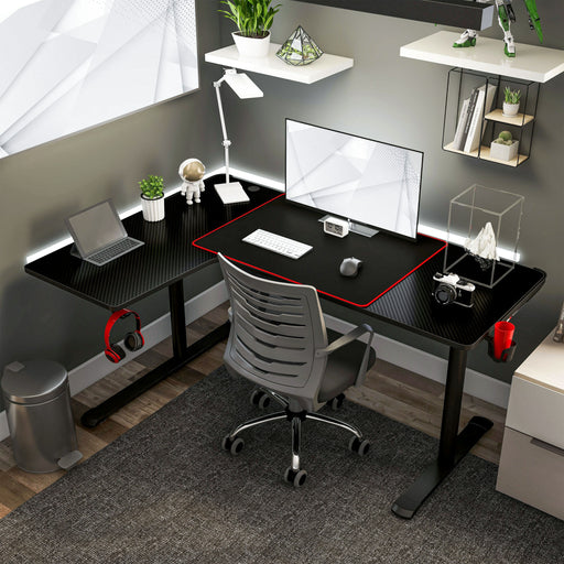 Left angled top view contemporary black L-shaped gaming desk with mouse pad in an office with accessories